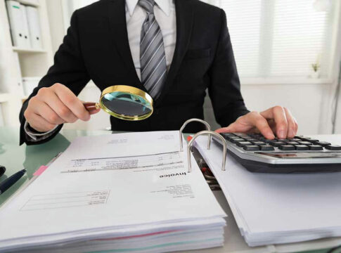 Person examining documents with magnifying glass and calculator.