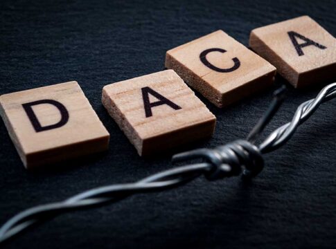 Wood letter tiles spelling DACA beside barbed wire on dark surface