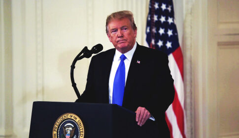 A man in a suit standing at a podium with the presidential seal, in front of an American flag