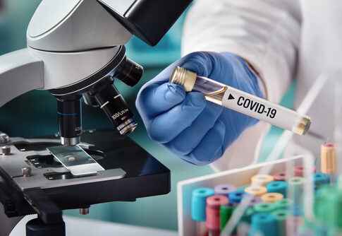 Scientist holding a test tube labeled COVID-19 next to a microscope