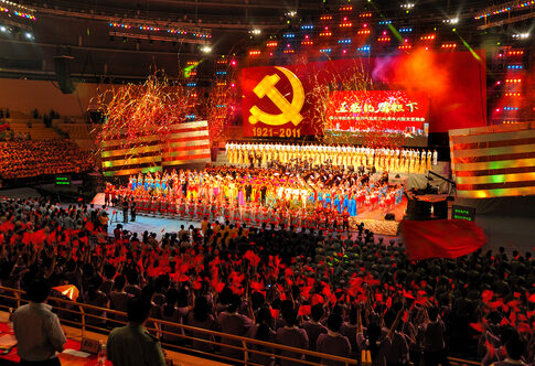 A large crowd at a celebratory event with performers on stage and fireworks in the background